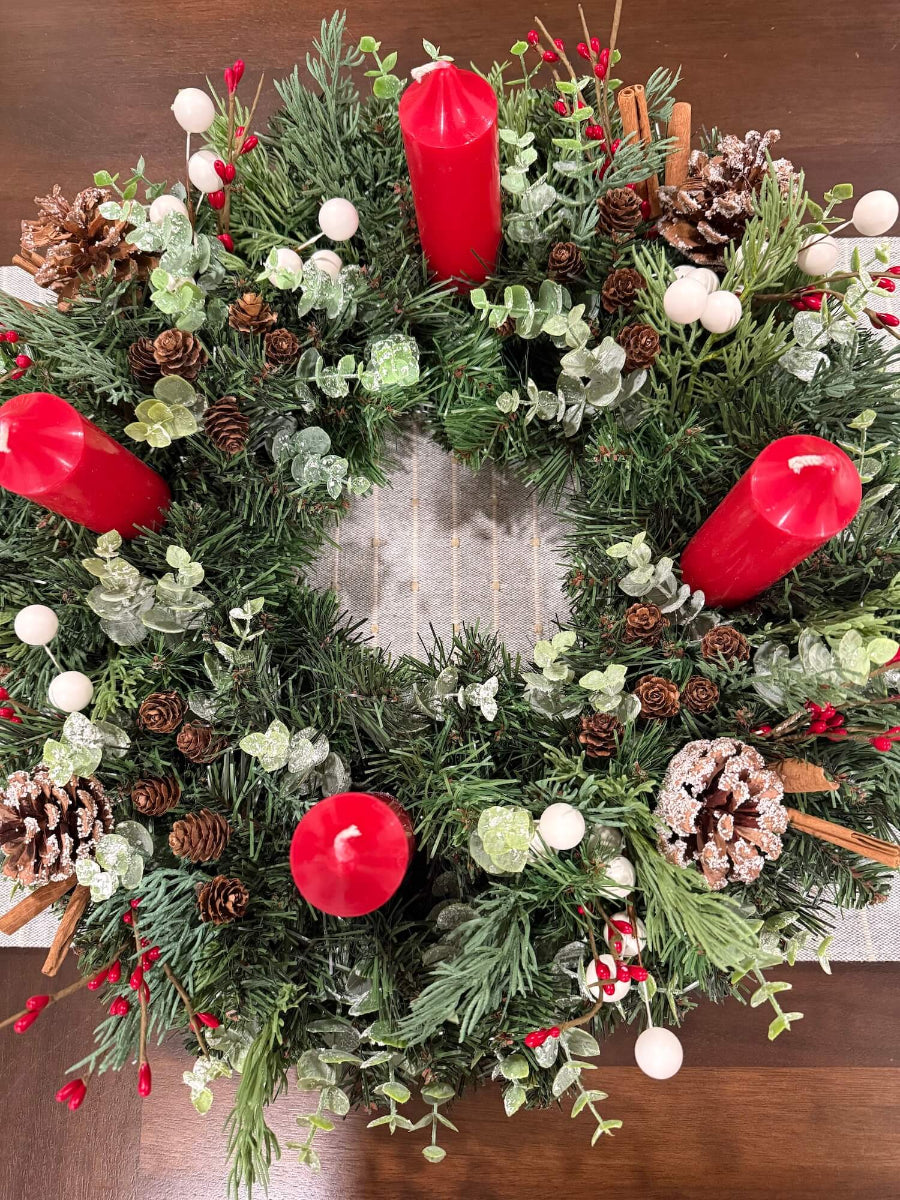 view from top for lush elegant handmade advent wreath with pine, arborvitae and snowy eucalyptus stems, with snowy and plain pinecones, cinnamon sticks, red and white berries, with short thick candles or purple/pink candles set on dining table