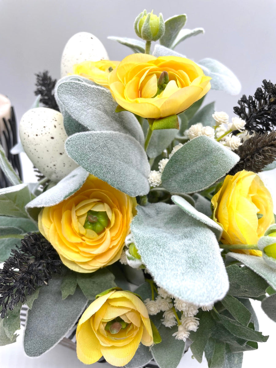 close up for easter arrangement with labs ear, yellow flowers, white flowers and faux eggs in black white metal can vase