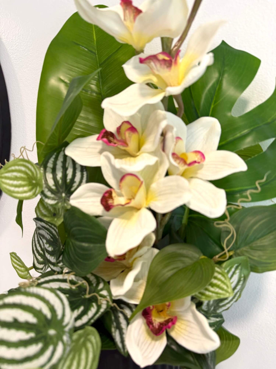 close up realistic looking tall faux white orchid arrangement accompanied with greenery in black matte textured ceramic vase