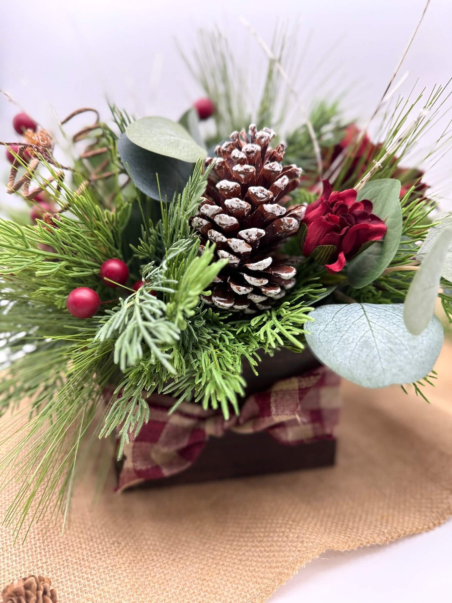 Decorative Christmas arrangement with pine cones, berries, and greenery in wooden vase