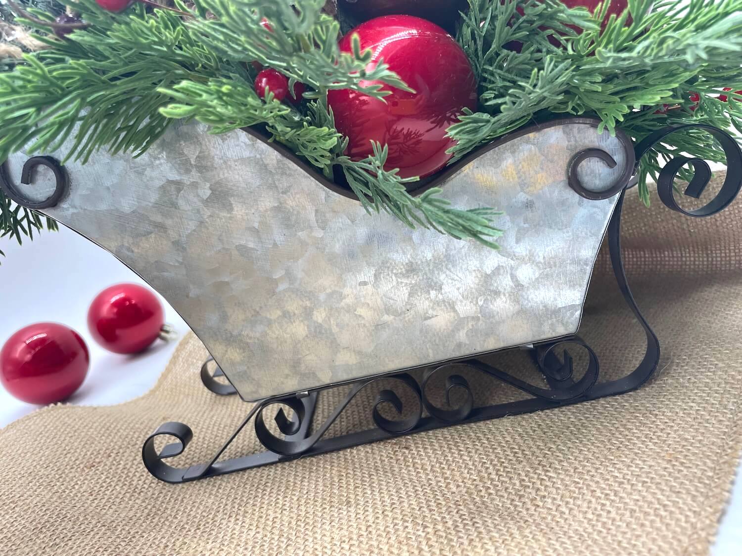 Decorative metal sleigh with variety of evergreen stems and christmas ornaments, pinecones and winter berries
