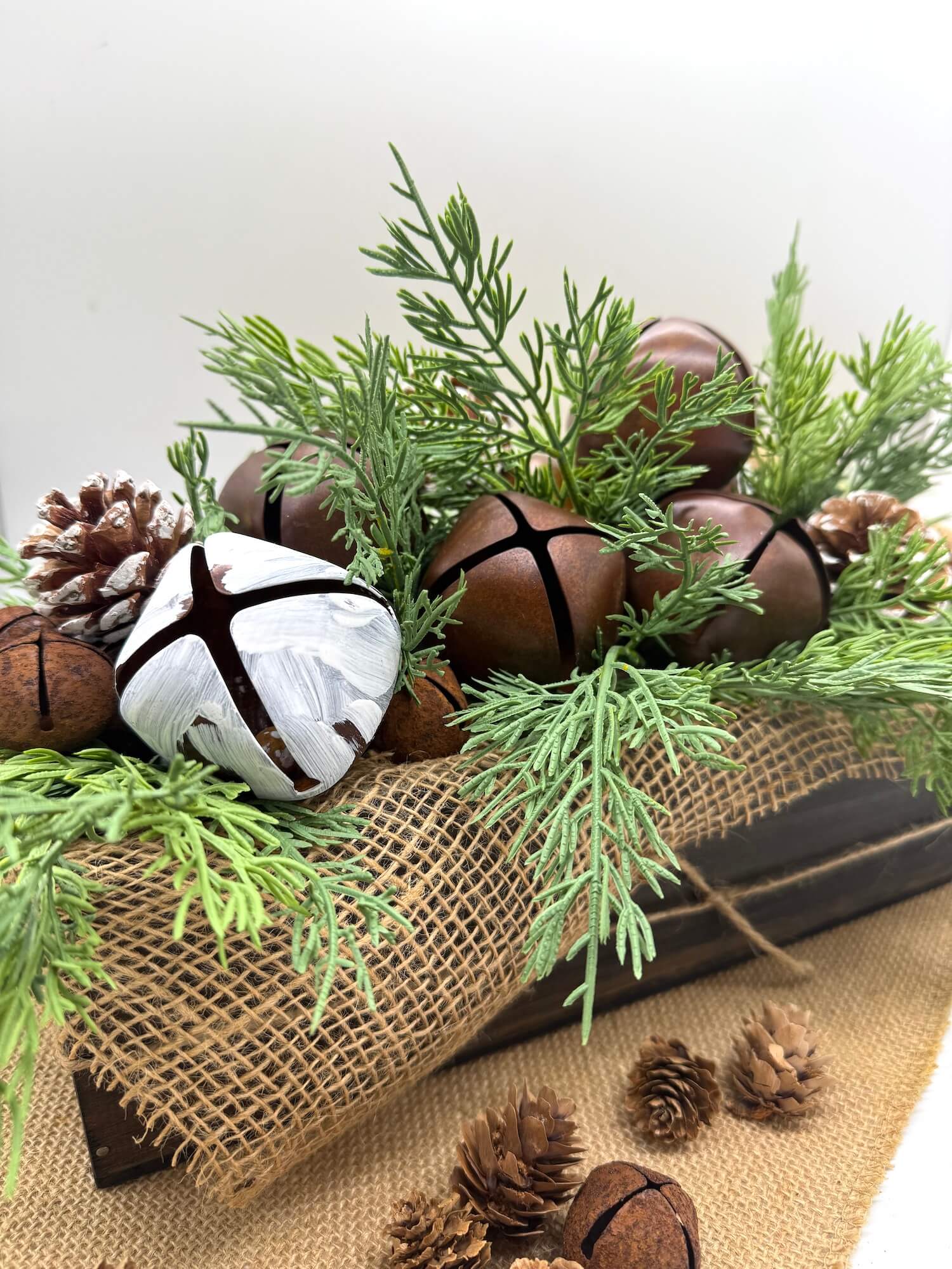 winter centerpiece with metal bells in brown and white, pinecones and evergreen in wooden vase box decorated with burlap, in modern farmhouse style