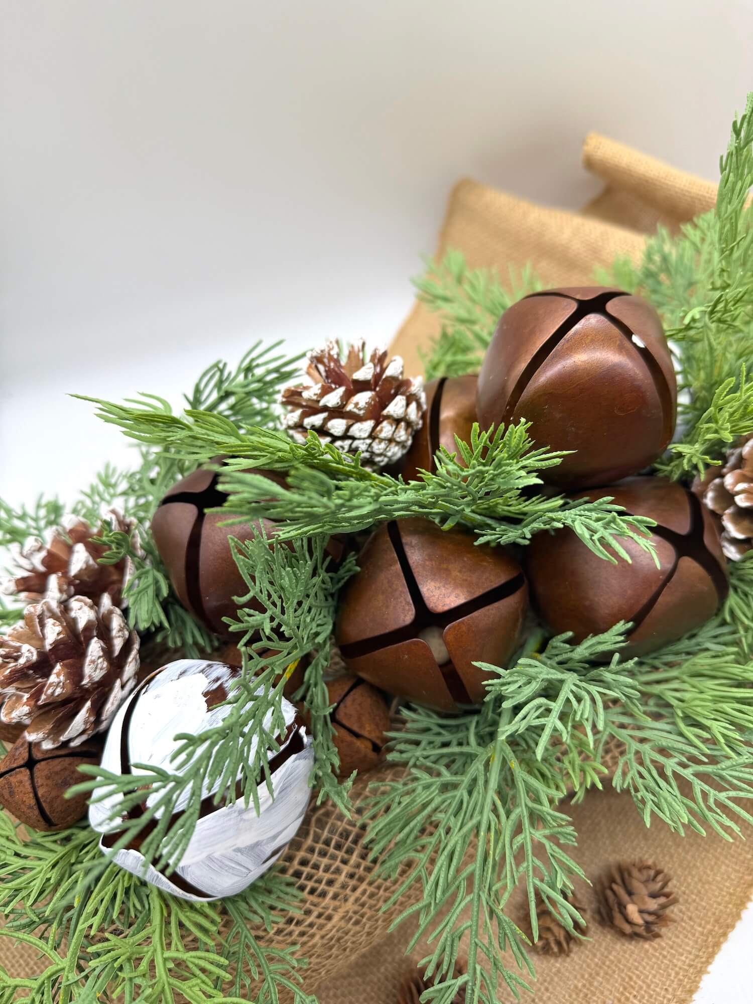 winter arrangement with metal bells, pinecones, evergreen stems in wooden planter is espresso color finished with burlap