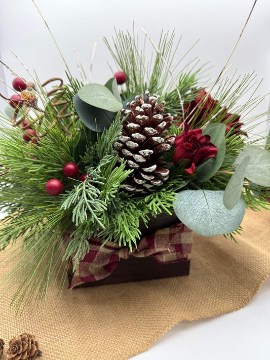 Christmas-themed floral arrangement with pine cones, berries, and greenery in wooden vase with burlap ribbon