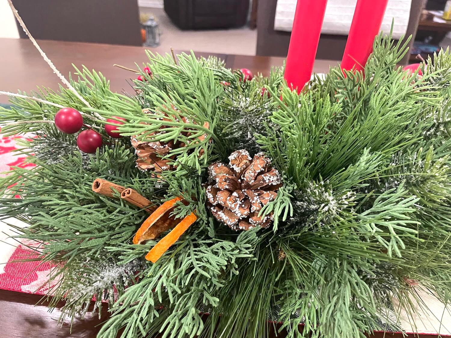 close up of another side of front of centerpiece with dried orange slices, cinnamon sticks, pinecones and variety of high quality greenery