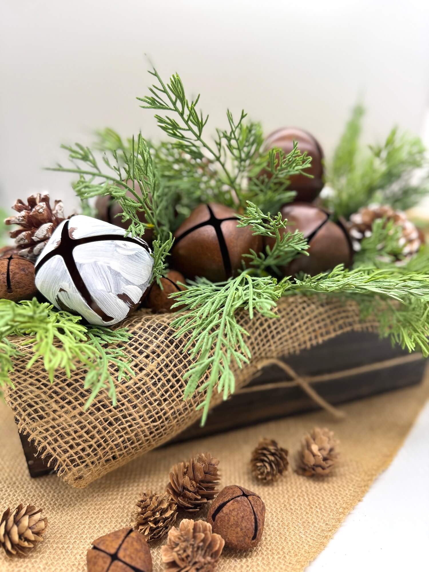 Decorative arrangement with greenery, pinecones, and metal bells in farmhouse style