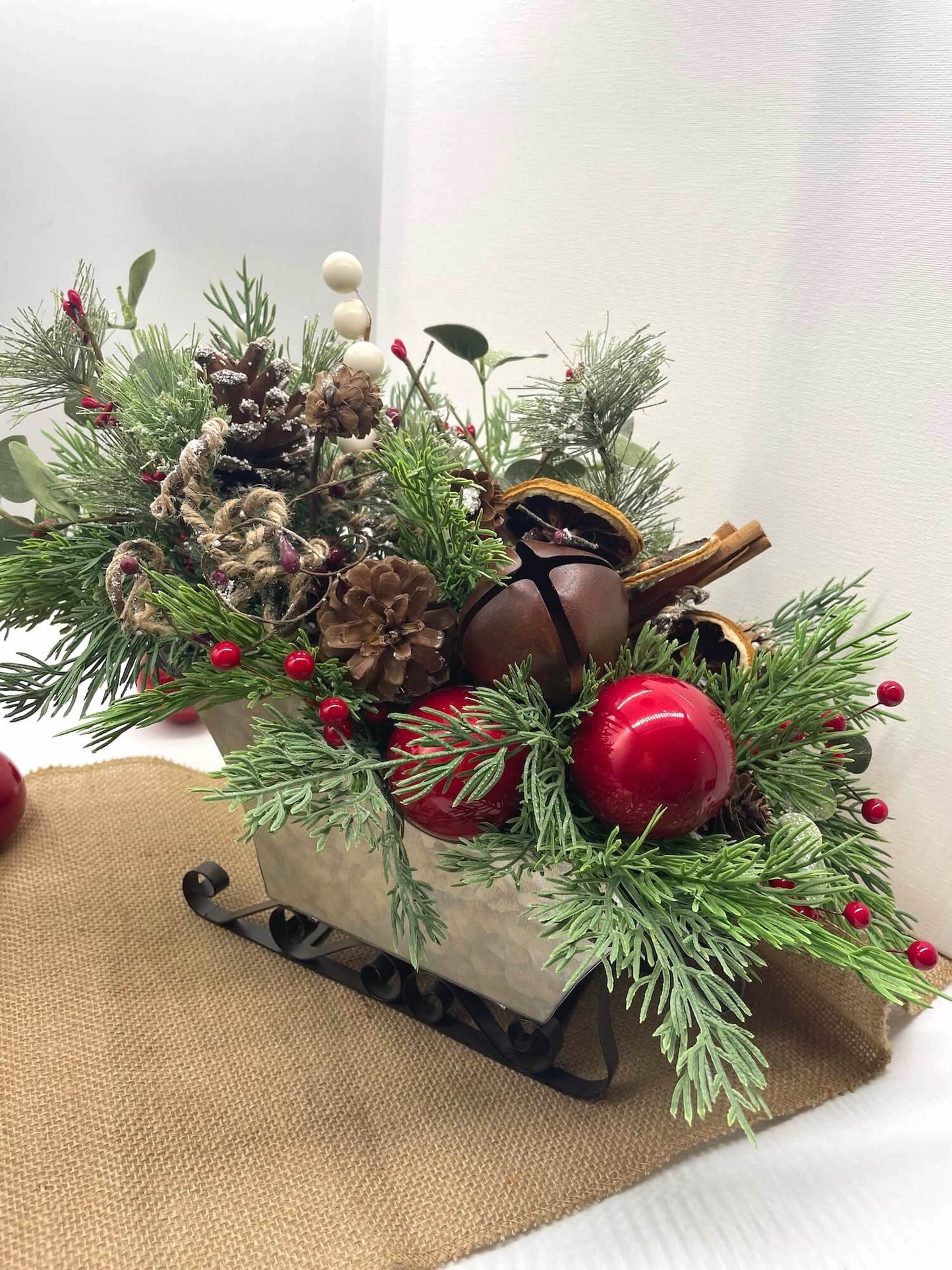 Decorative Christmas arrangement with greenery, red ornaments, and pinecones in metal sled vase