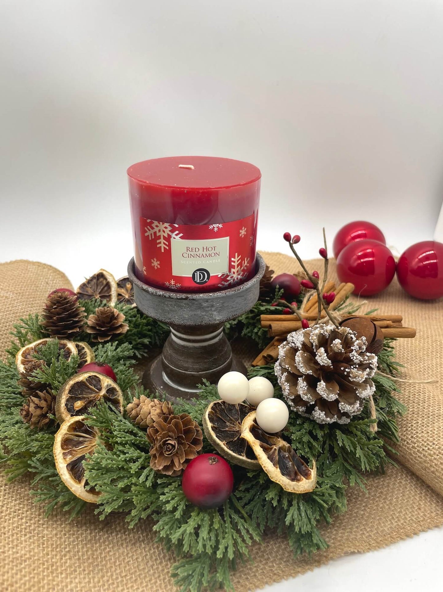small evergreen table wreath with pine cones, dried oranges, cinnamon stick and a red candle