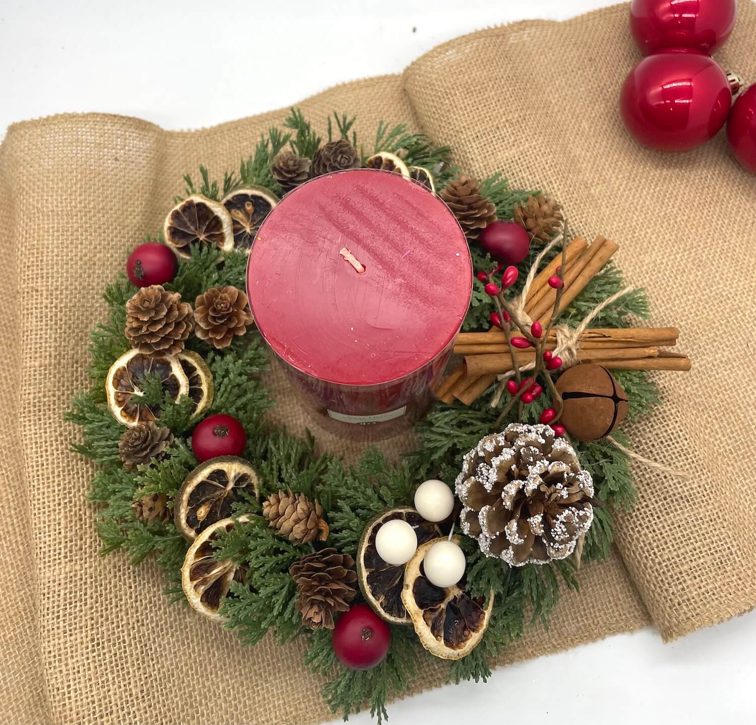 view from top of small evergreen table wreath with pine cones, dried oranges, cinnamon stick and a red candle with red pillar candle