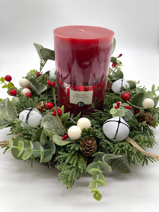 small evergreen winter table wreath with greenery, white metal bells, pinecones and winter berries and red pillar candle in the middle