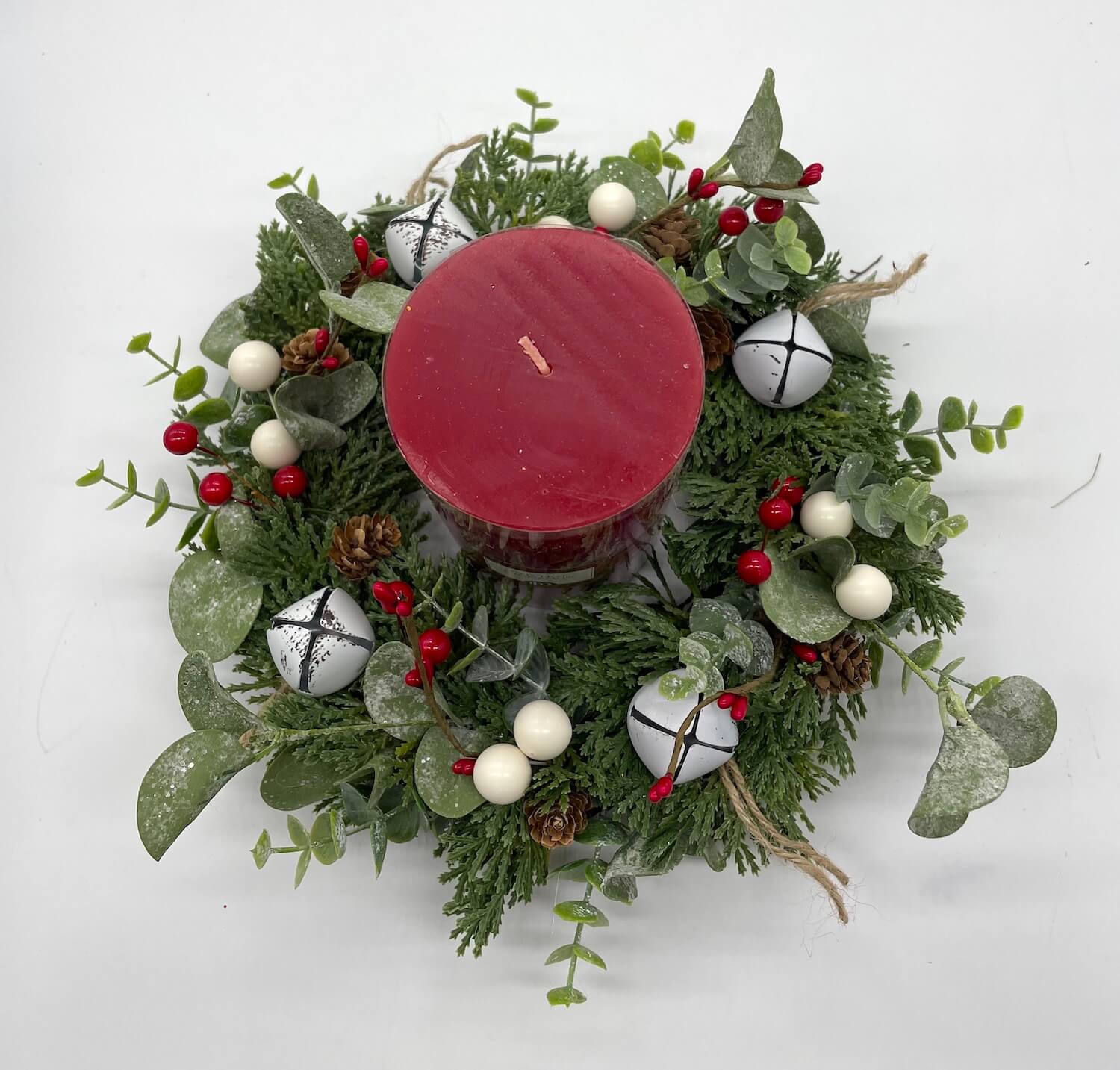 Decorative christmas table wreath with a red candle, greenery, berries, white bells, pinecones 