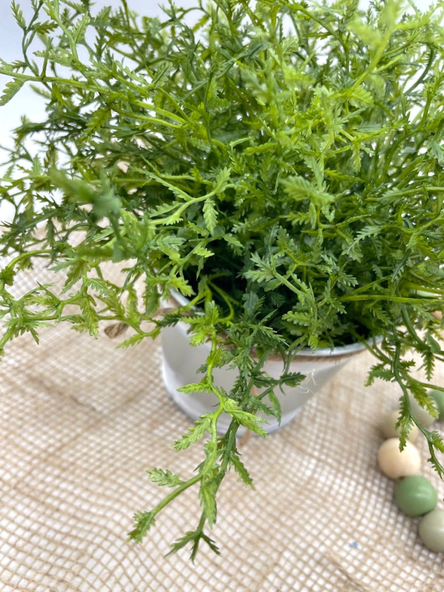 close up for vivid green faux plant fern in metal pot touched with white paint and decorated with jute