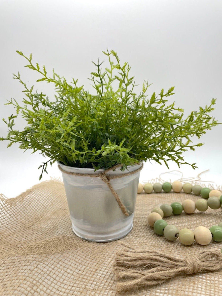 vivid green faux plant fern in metal pot touched with white paint and decorated with jute
