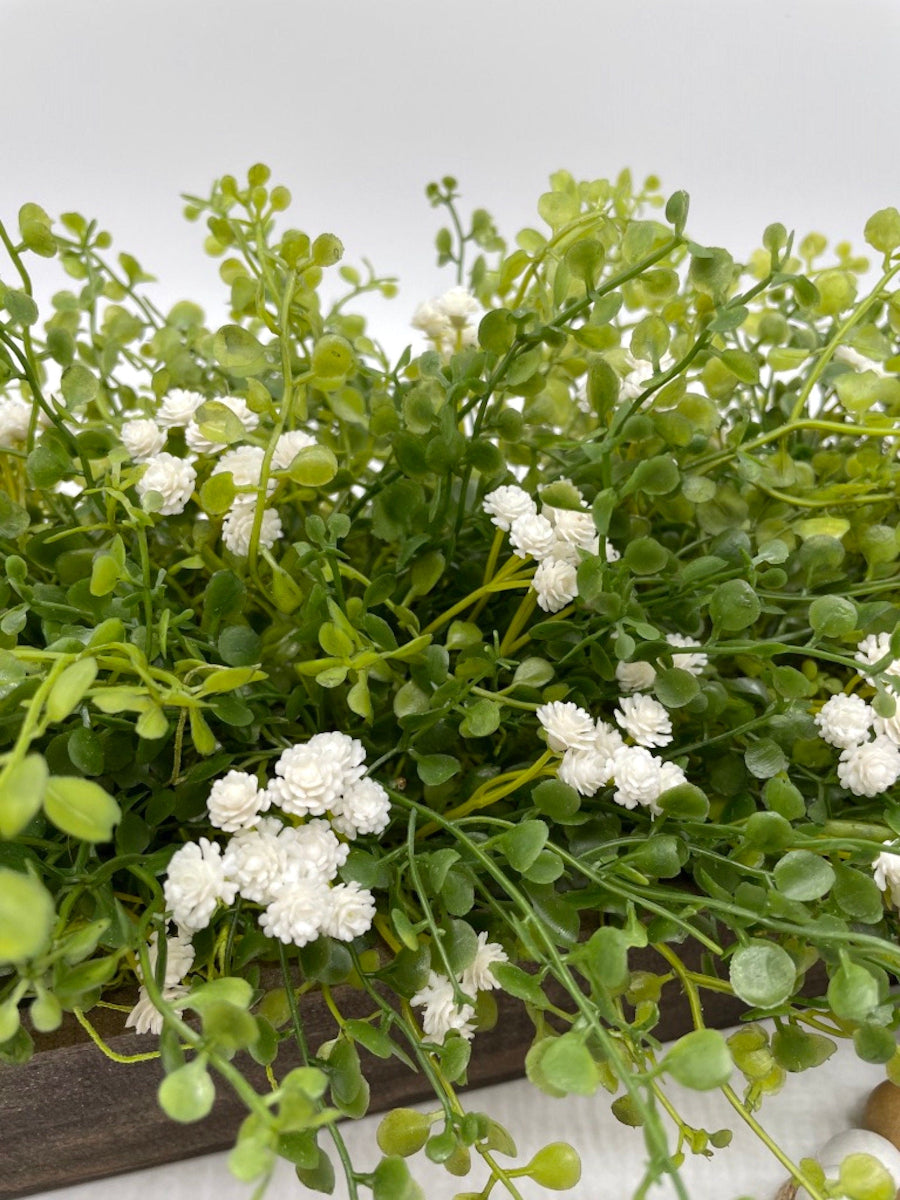 close up for vivid green realistic looking faux greenery with white flowers in long wooden planter stained is expresso color