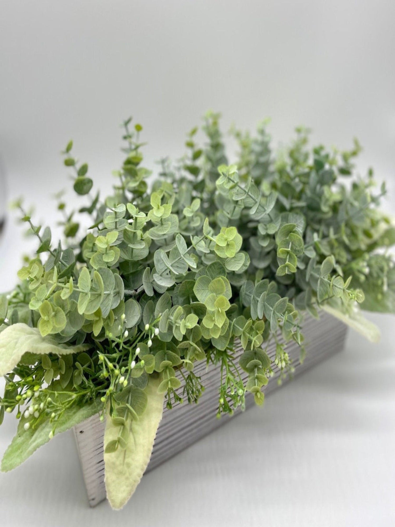 realistic looking faux eucalyptus with lambs ear leaves and delicate white flowers in whitewashed wooden planter box