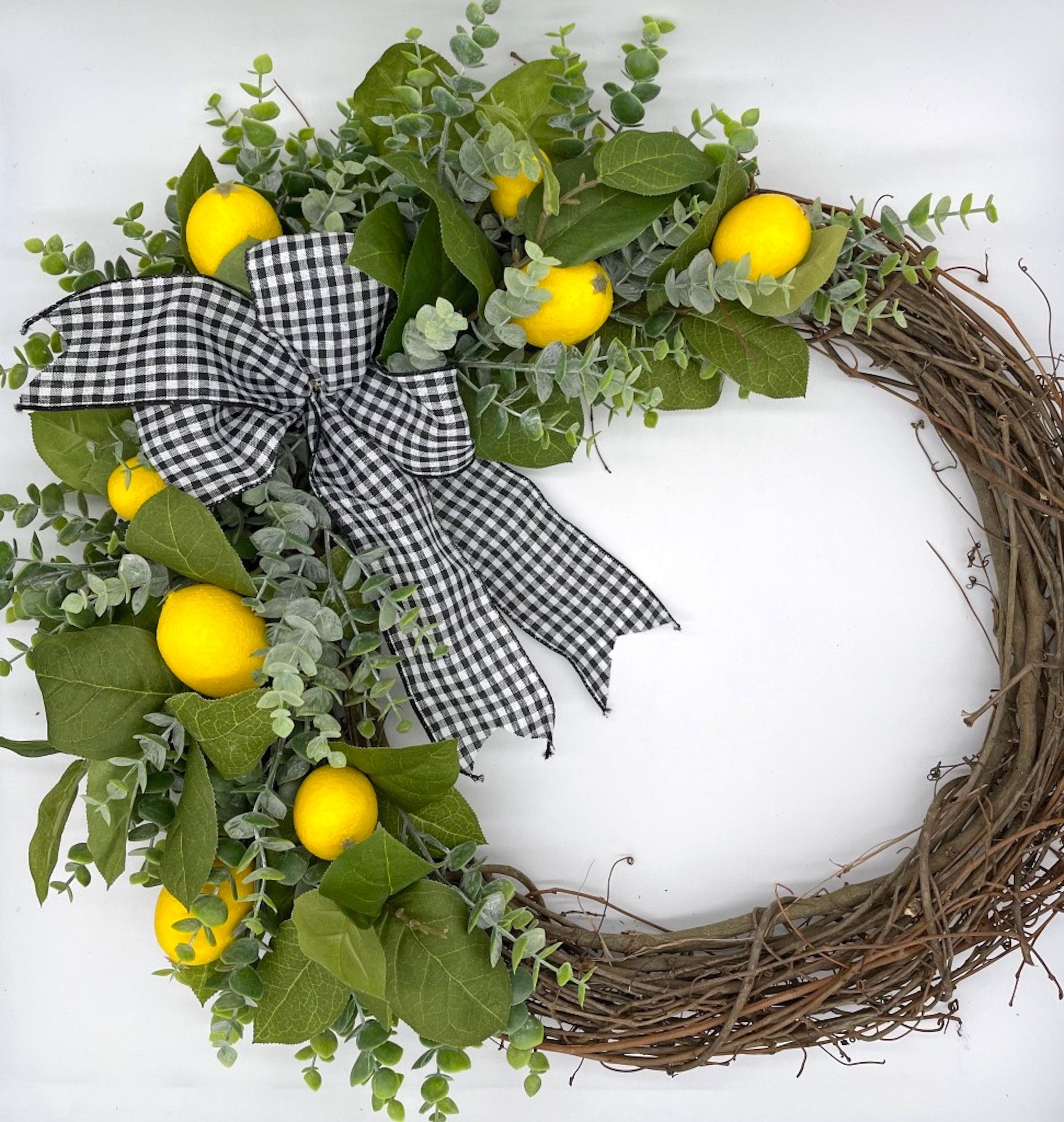 lemon wreath with green leaves and eucalyptus stems on grapevine round base decorated with black and white checkered bow