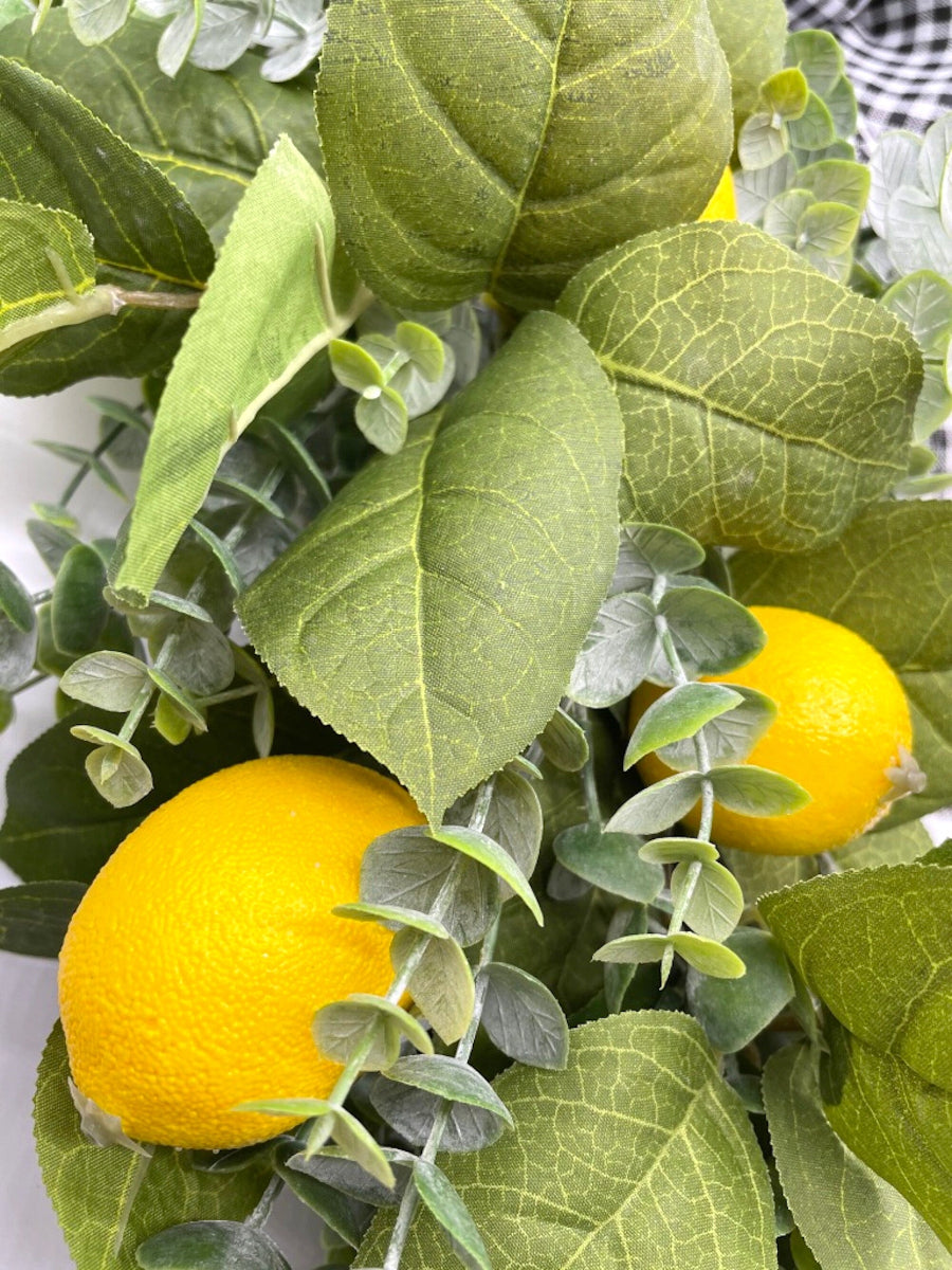 close up for lemon wreath with green leaves and eucalyptus stems on grapevine round base decorated with black and white checkered bow