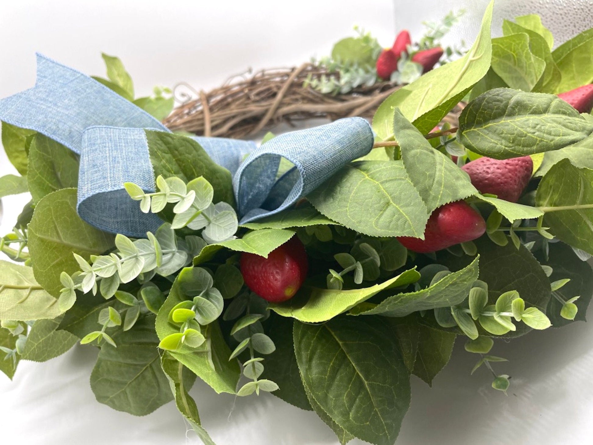 realistic strawberry wreath with greenery and faux berries on a round grapevine base and periwinkle bow