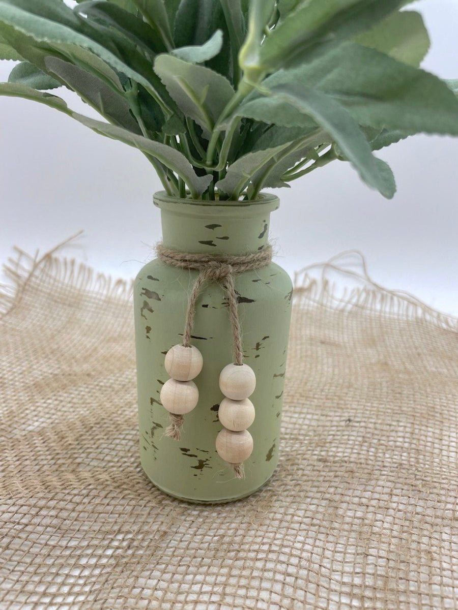 close up for realistic looking faux sage arrangement in bottle vase painted in green sage and distressed, decorated with jute and wooden beads